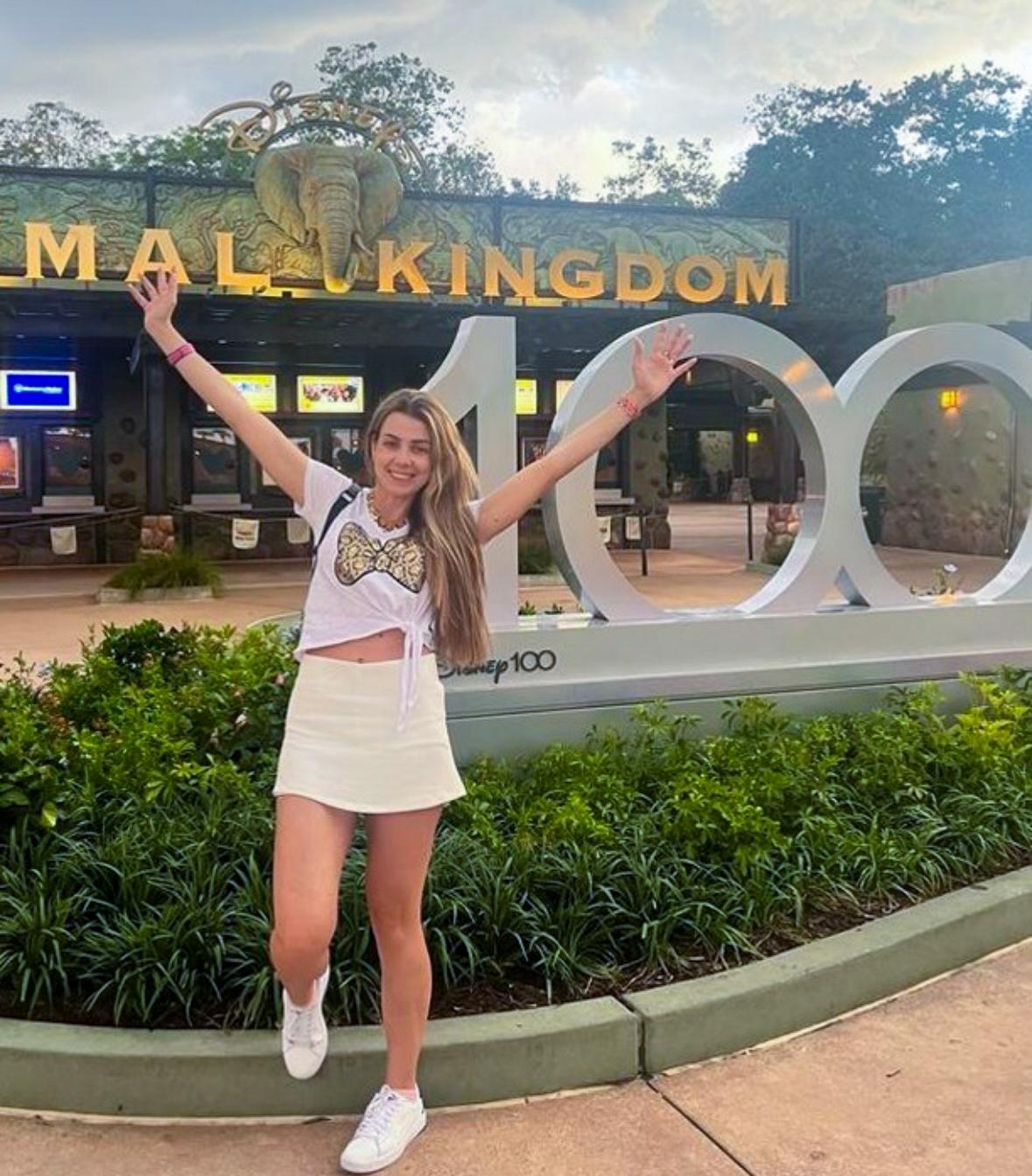 Woman celebrating at Disney’s Animal Kingdom entrance with festive “100” display and greenery.