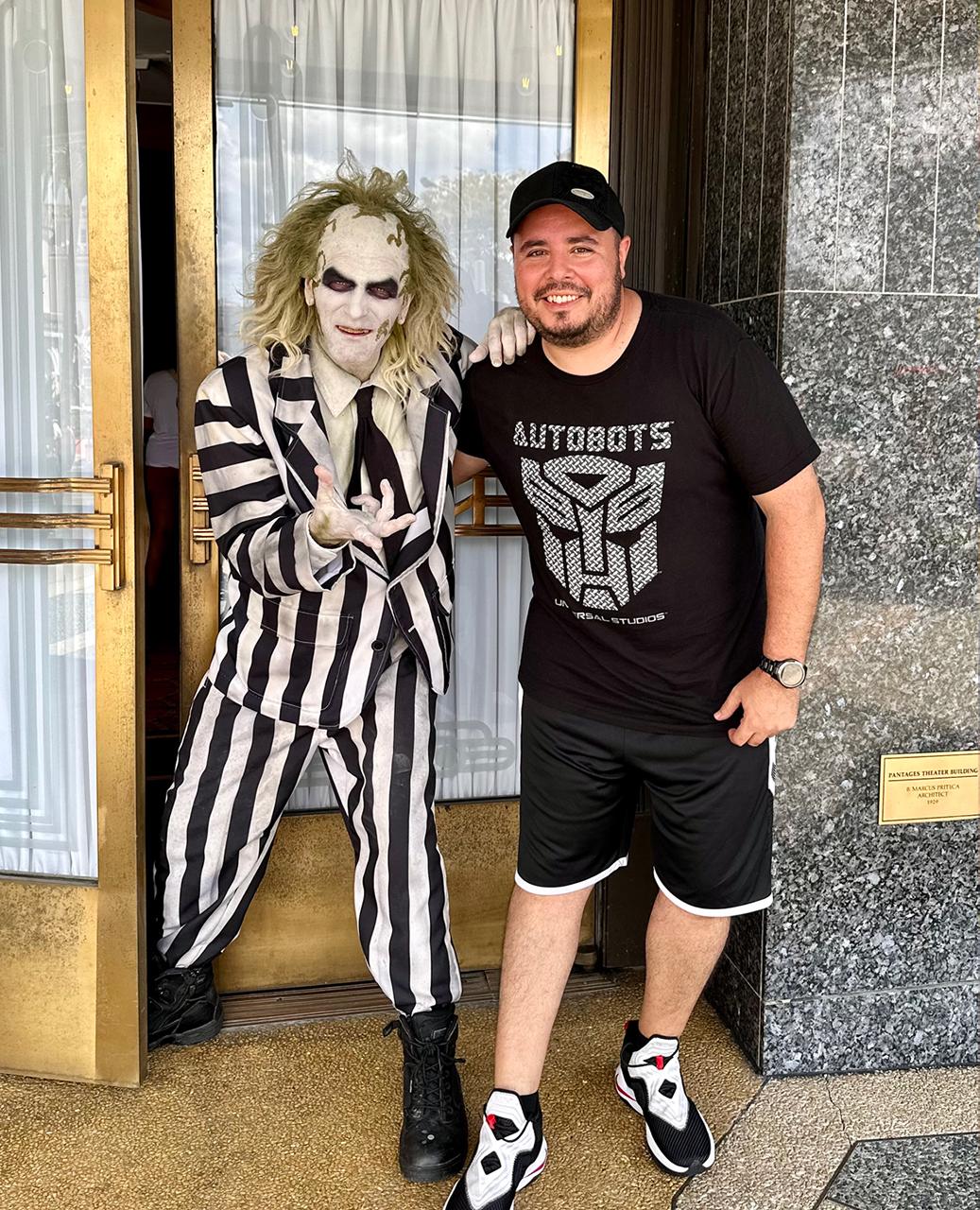 Fan posing with Beetlejuice in striped suit at theme park entrance