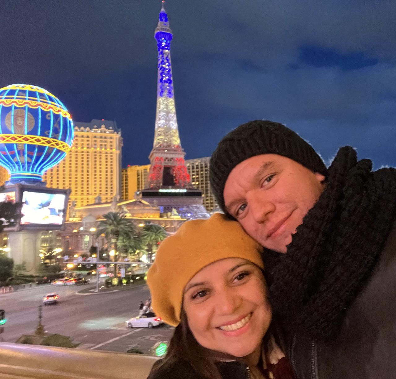 Smiling couple on Las Vegas Strip at night with Eiffel Tower and city lights.