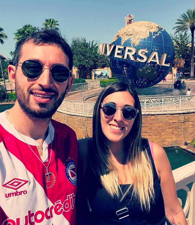 Smiling couple posing at Universal Studios globe with palm trees and sunny theme park backdrop.