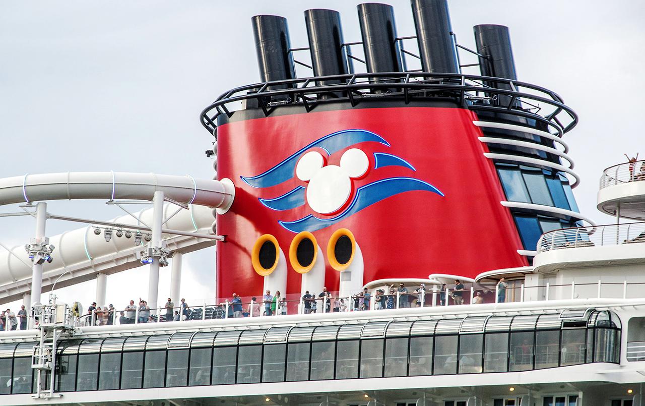 Disney Cruise Line ship funnel with Mickey Mouse silhouette and guests enjoying the deck.