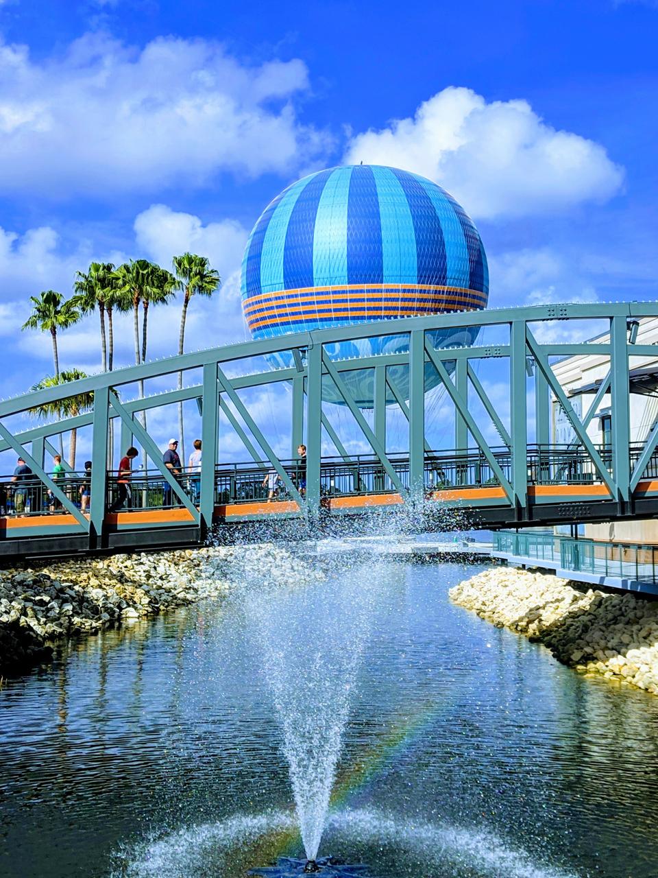 Blue hot air balloon over bridge, fountain, and palm trees at Disney Springs.