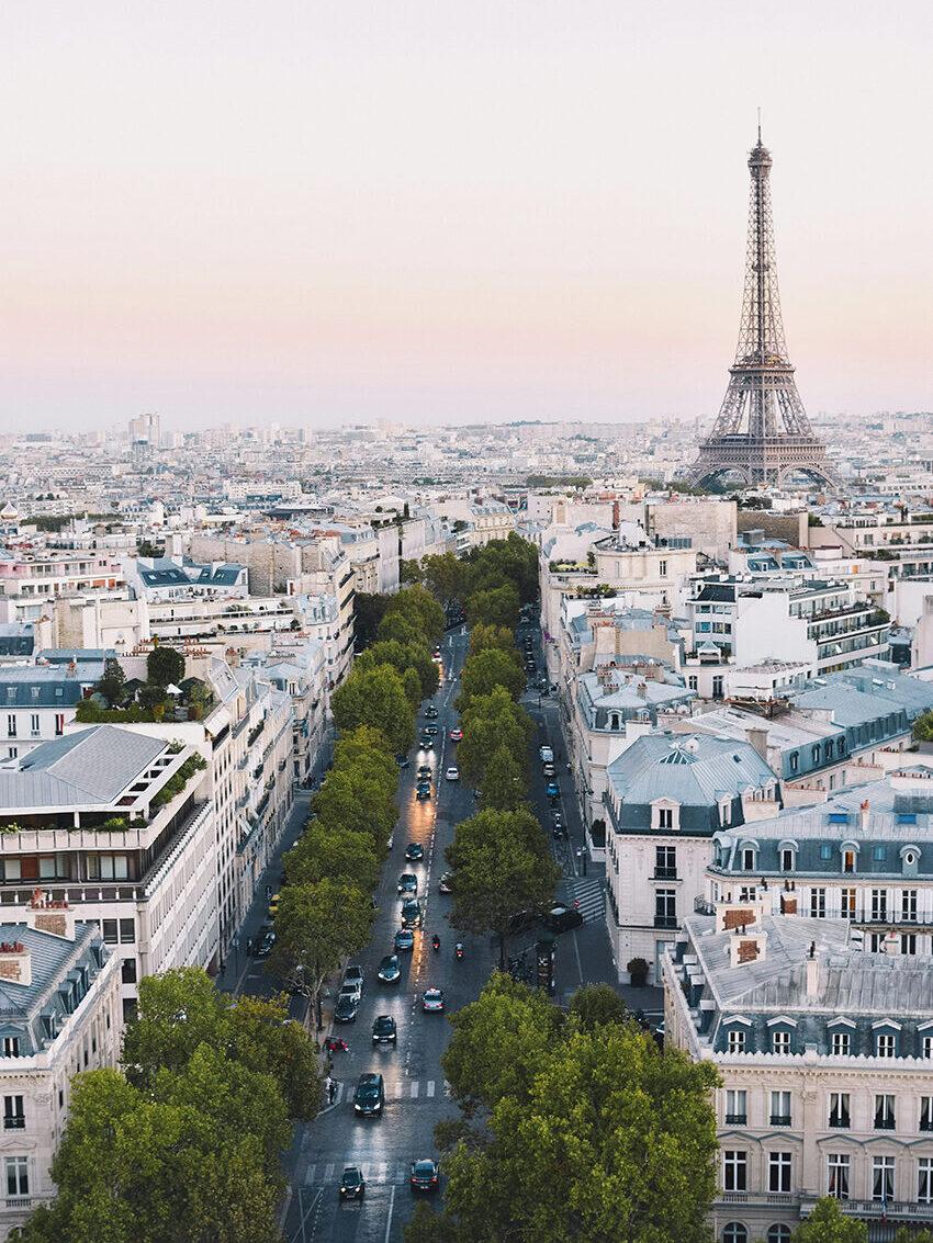Aerial view of Eiffel Tower at sunset with Paris rooftops and city skyline.