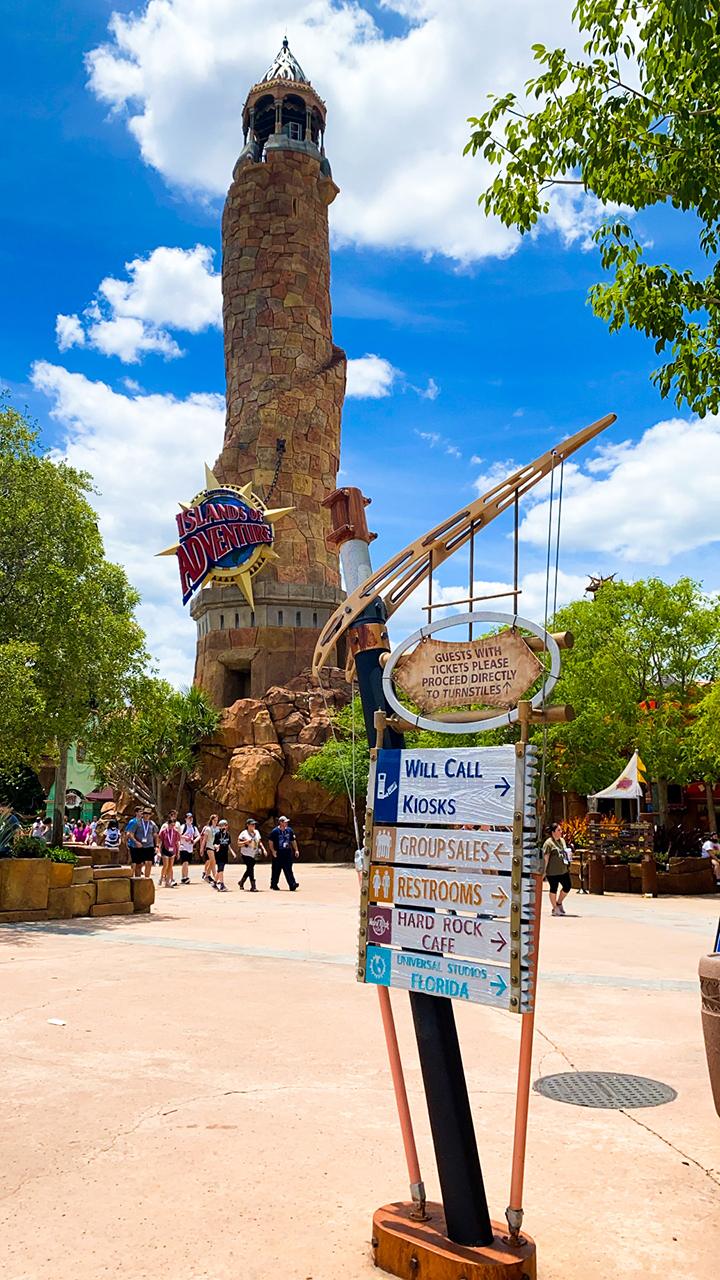 Islands of Adventure entrance tower with nautical design, themed signage, and visitors under blue sky.