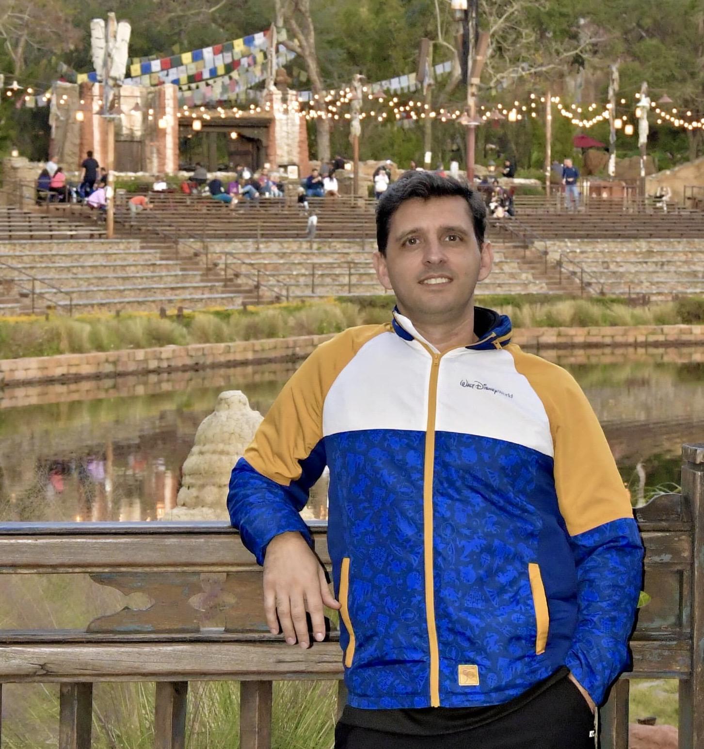 Man by serene pond with prayer flags and greenery in festive outdoor setting.