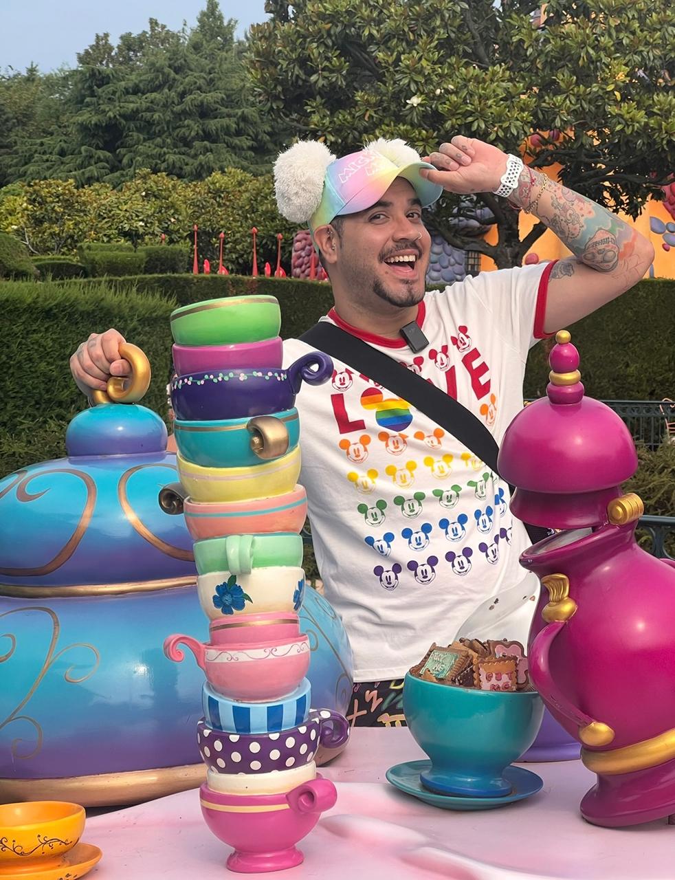Man smiling at colorful teacup theme park with oversized teapots and playful decorations.