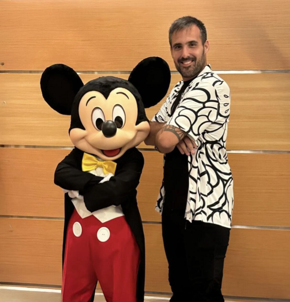 Man posing with Mickey Mouse in classic outfit at Disney event
