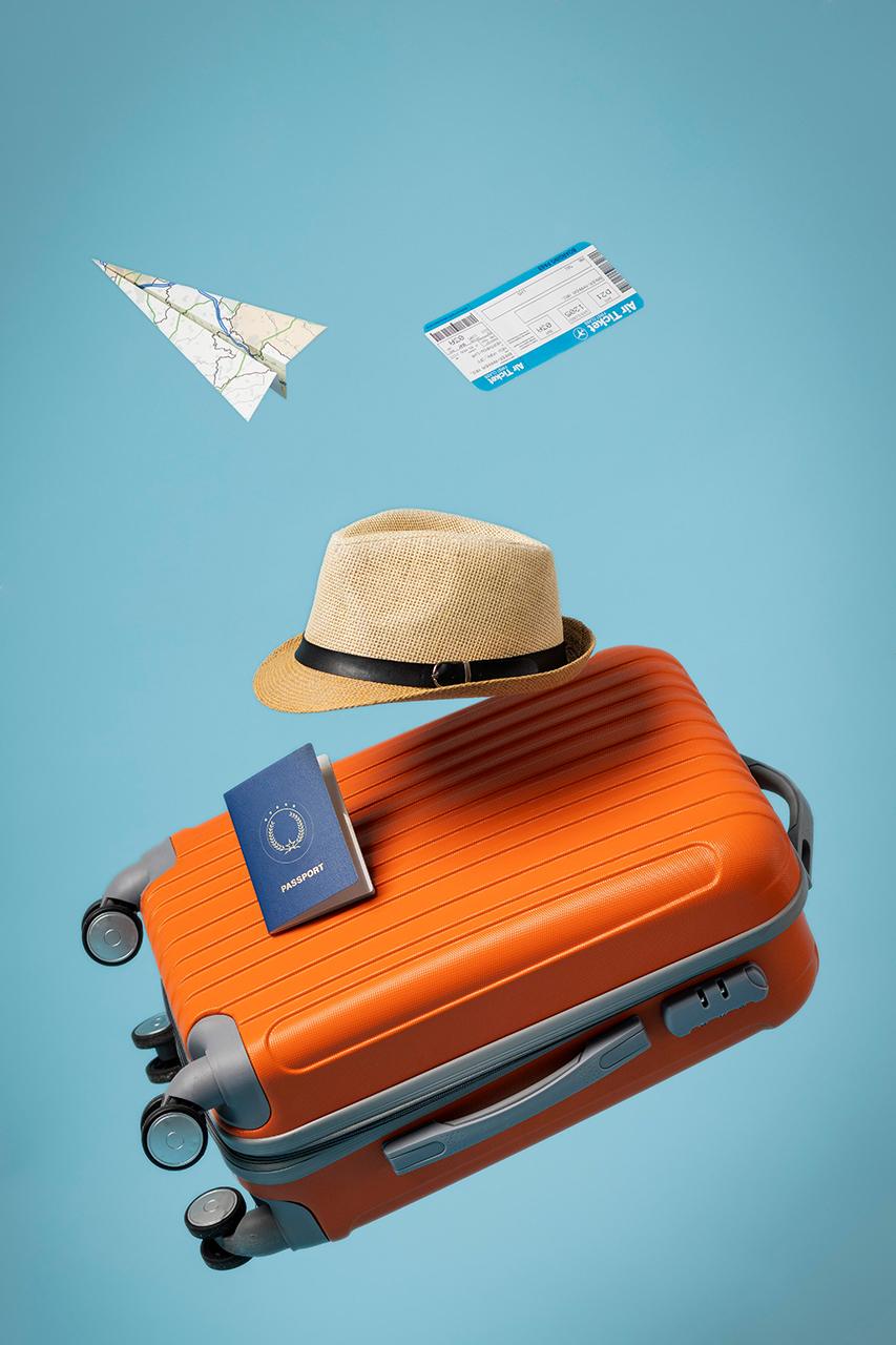 Orange travel suitcase with straw hat, passport, and paper airplanes on blue background.