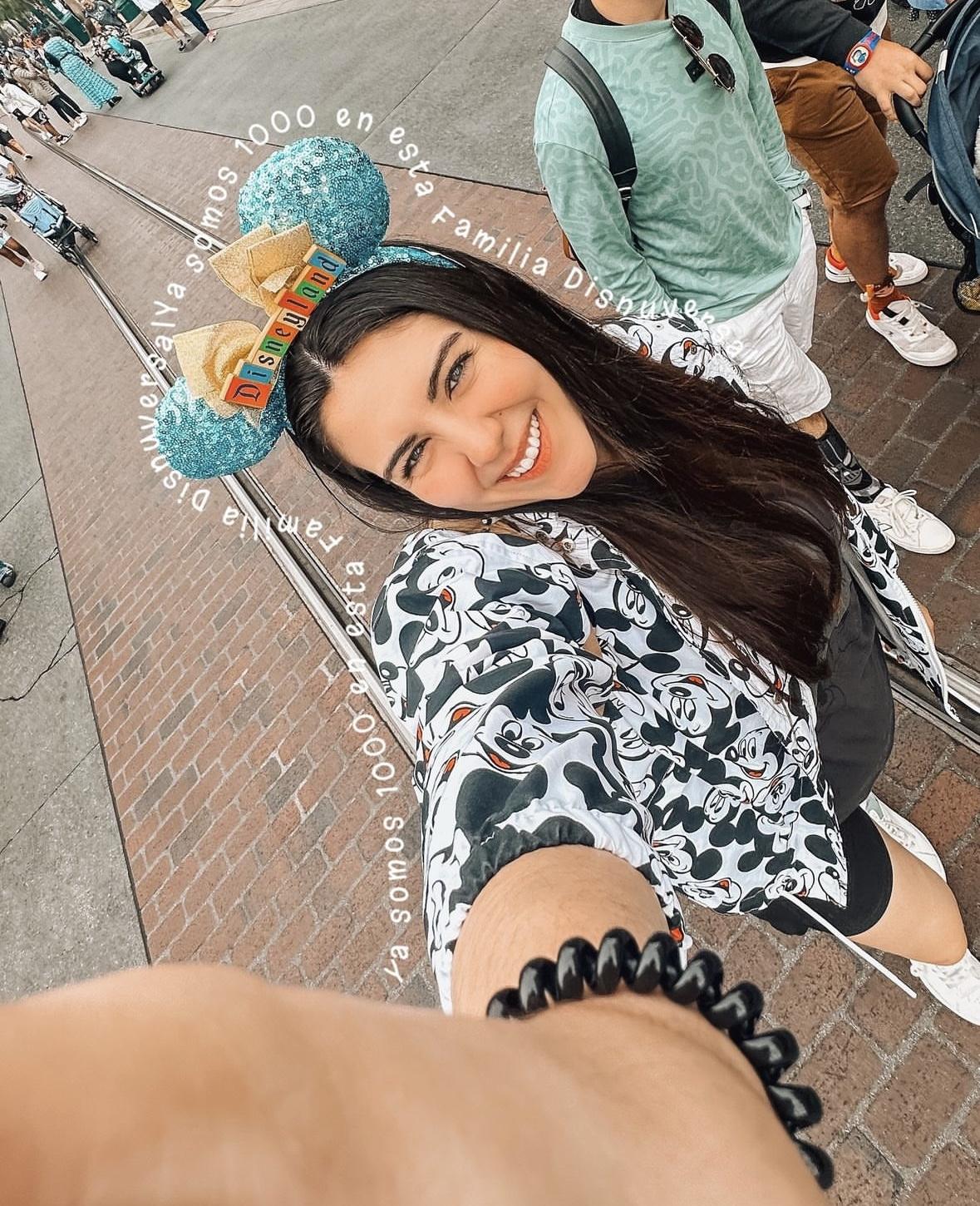 Woman smiling in Minnie Mouse ears selfie at Disney theme park.