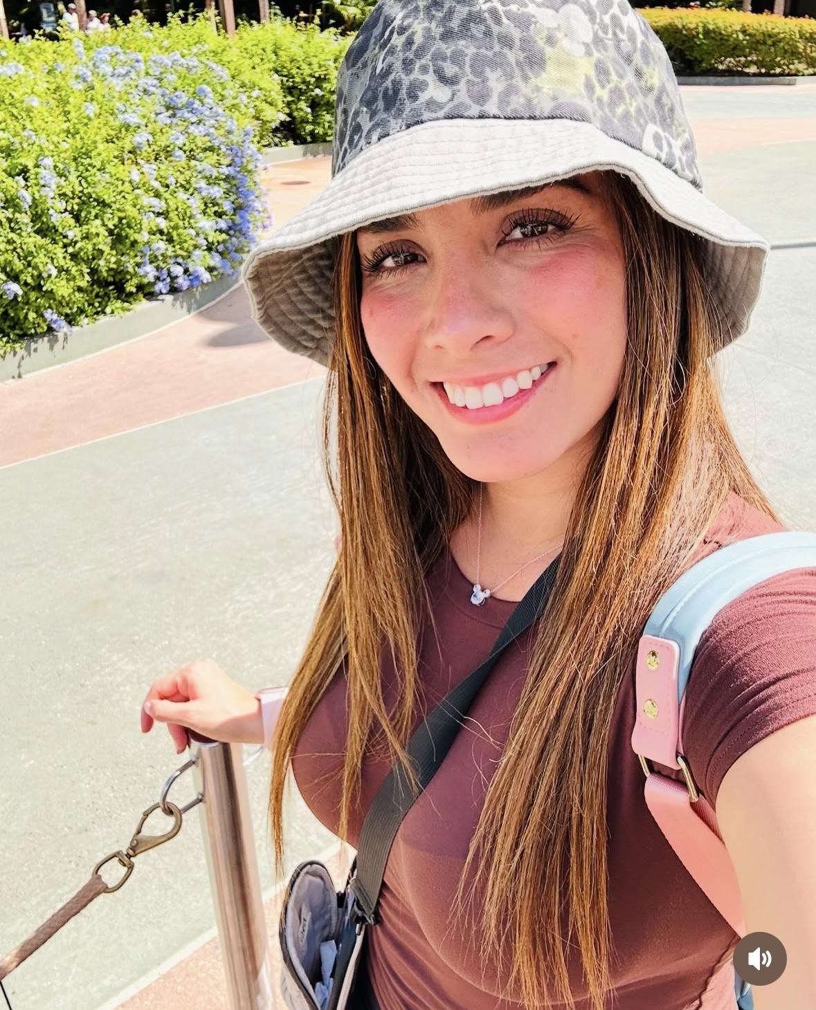 Smiling woman in leopard bucket hat taking selfie with blue flowers and greenery outdoors