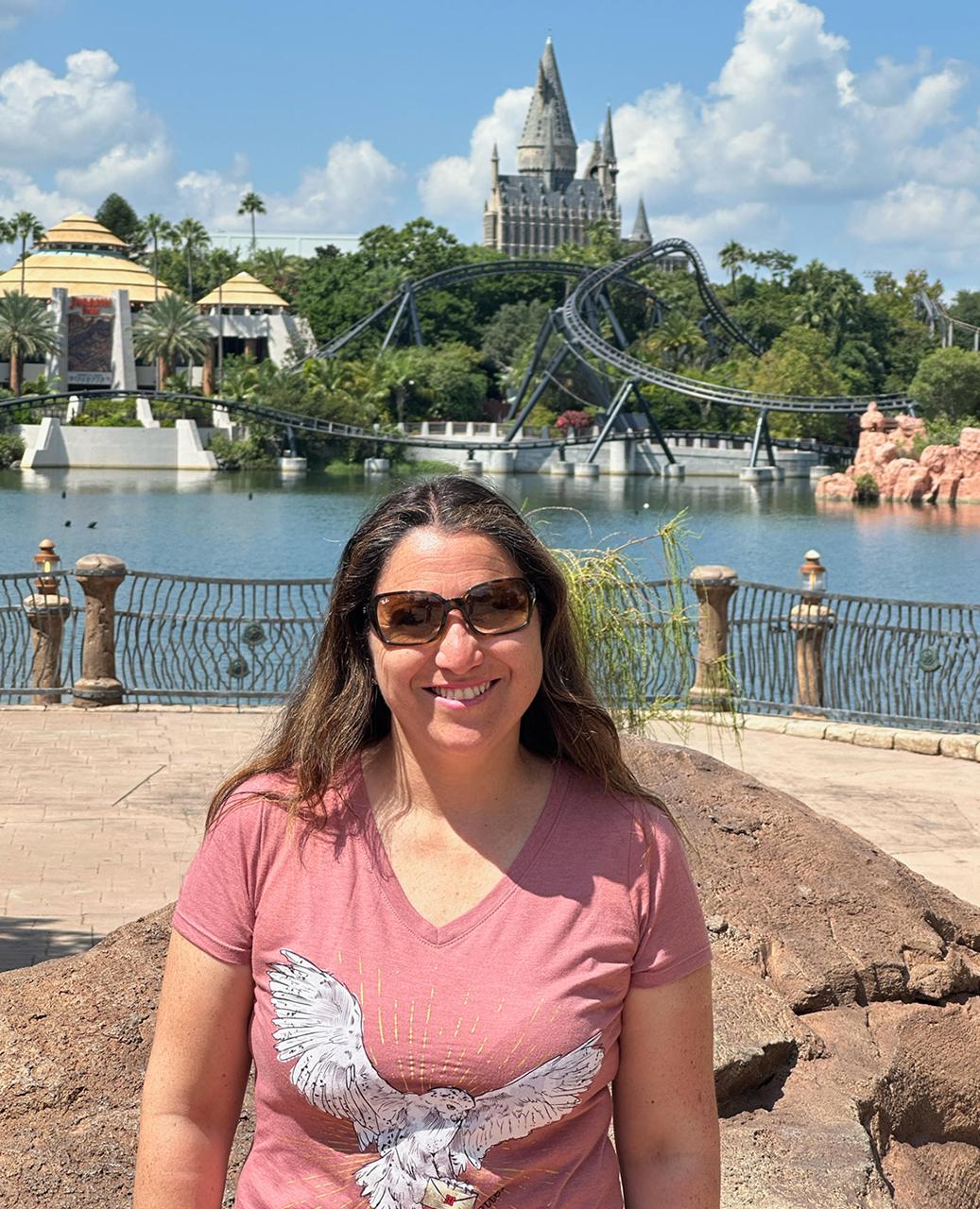 Woman smiling at theme park with fairytale castle and roller coaster in background