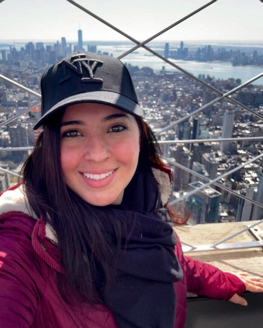 Smiling woman on Empire State Building observation deck with New York City skyline view.