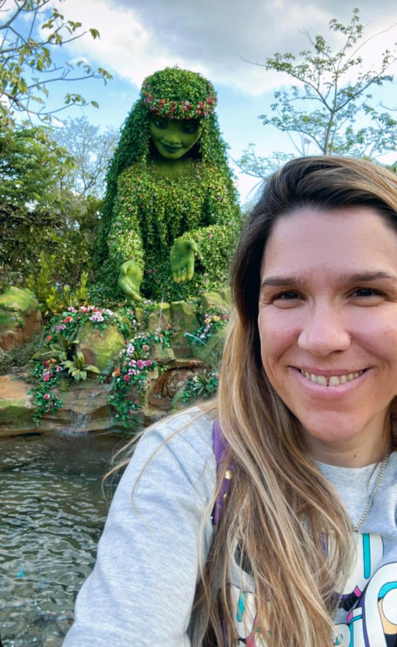 Smiling woman with serene garden topiary sculpture surrounded by lush greenery and flowers.
