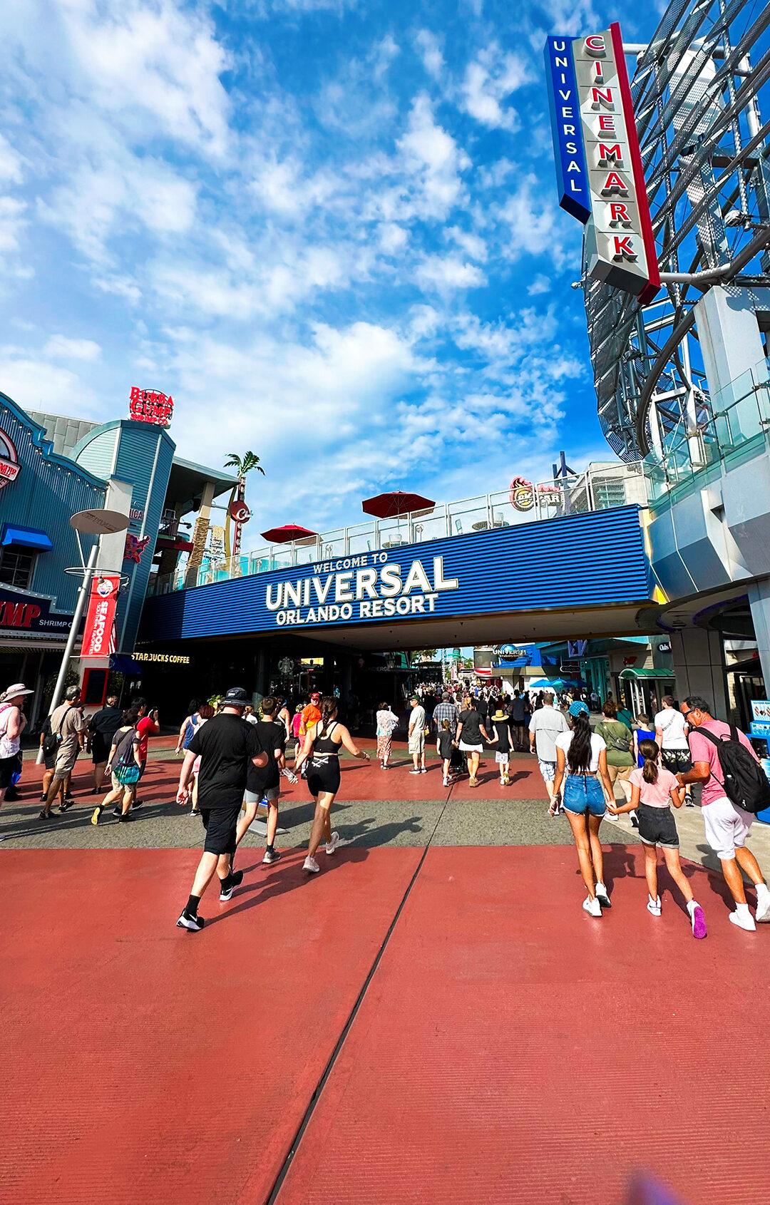 Crowds enter Universal Orlando Resort under sunny skies near the iconic Universal sign.