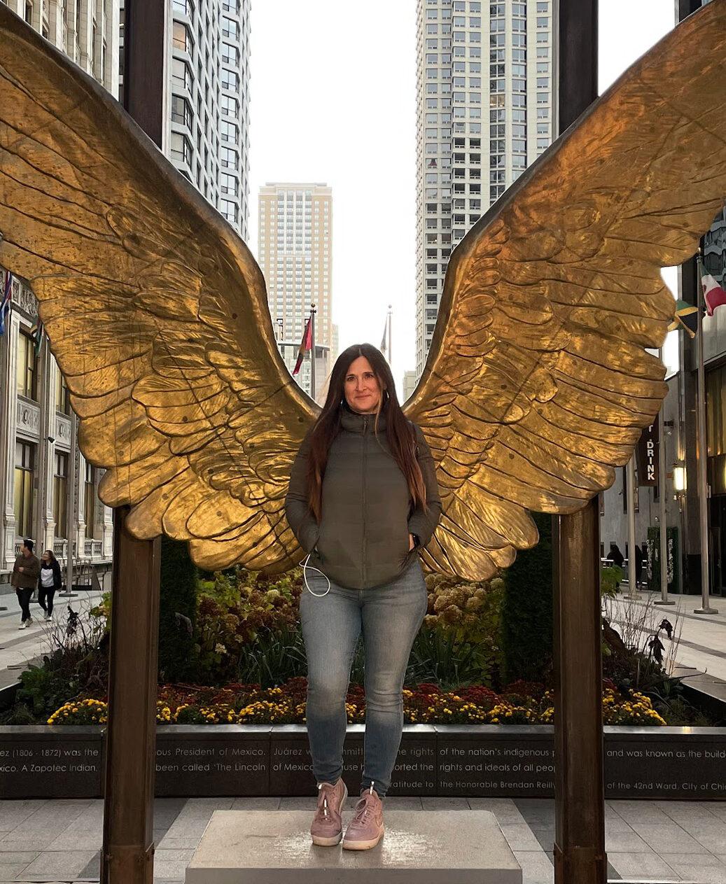 Woman posing with golden angel wings sculpture in urban city setting