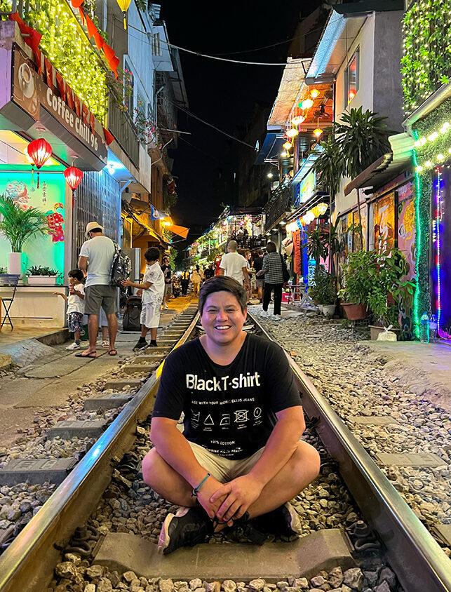 Smiling young man on night market railway with colorful lights and lively crowds