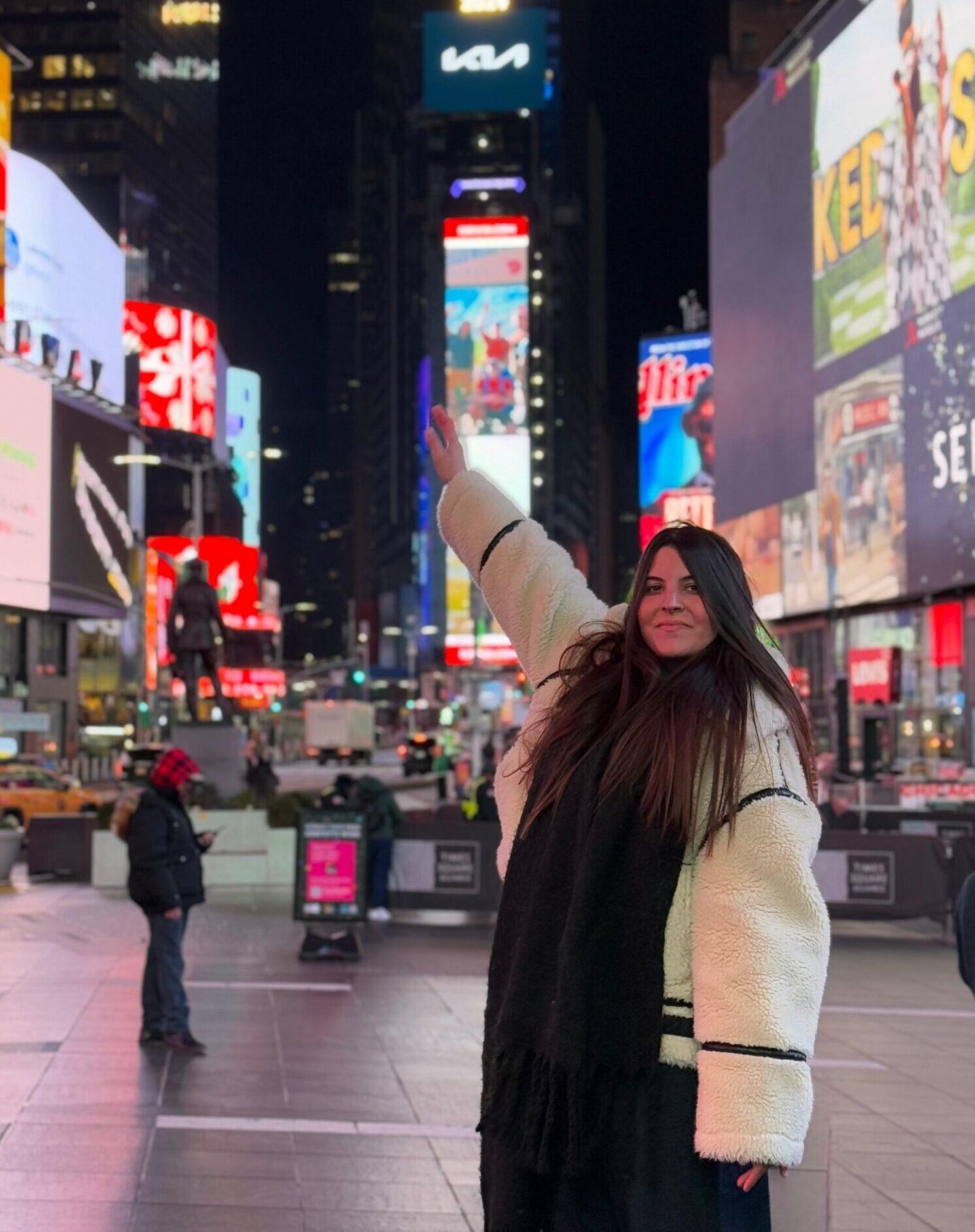 Smiling woman celebrating in Times Square at night with bright neon billboards.
