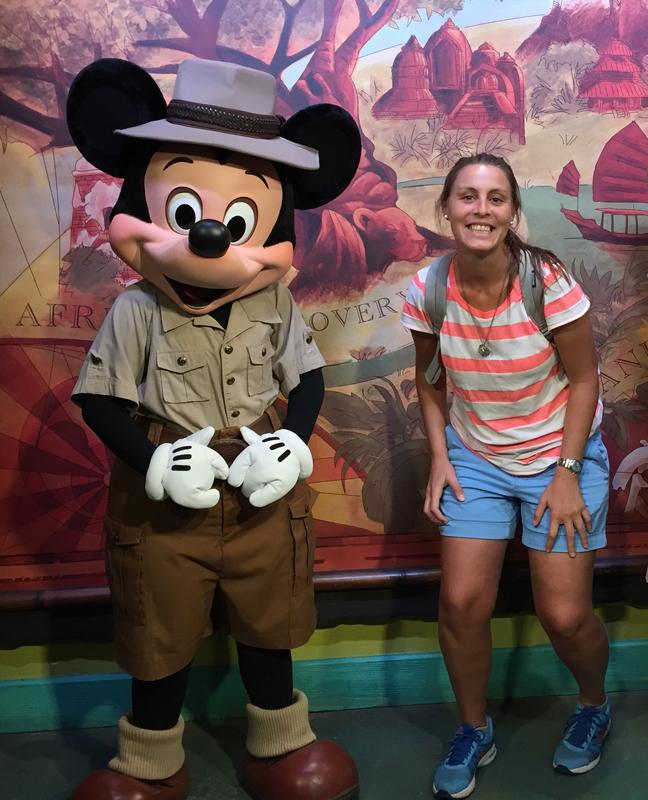 Woman smiling with famous cartoon explorer character in colorful theme park adventure setting.
