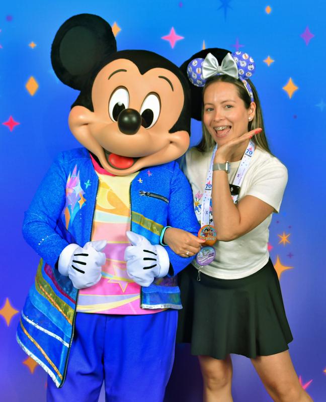 Woman posing with Mickey Mouse at Disney theme park under starry blue backdrop.