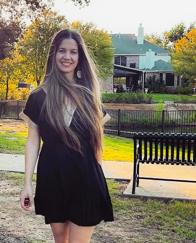 Smiling woman in black dress posing in sunny autumn park with colorful foliage.